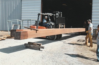 Forklift handling a large tropical hardwood timber outside a workshop