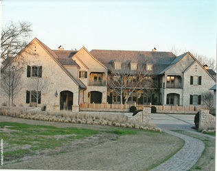 Stone estate home with a natural wood shake roof, gables, and a landscaped approach